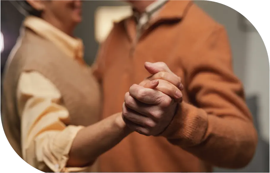 An older couple shares a heartfelt dance in a charming room, radiating trust and affection in their joyful expressions.